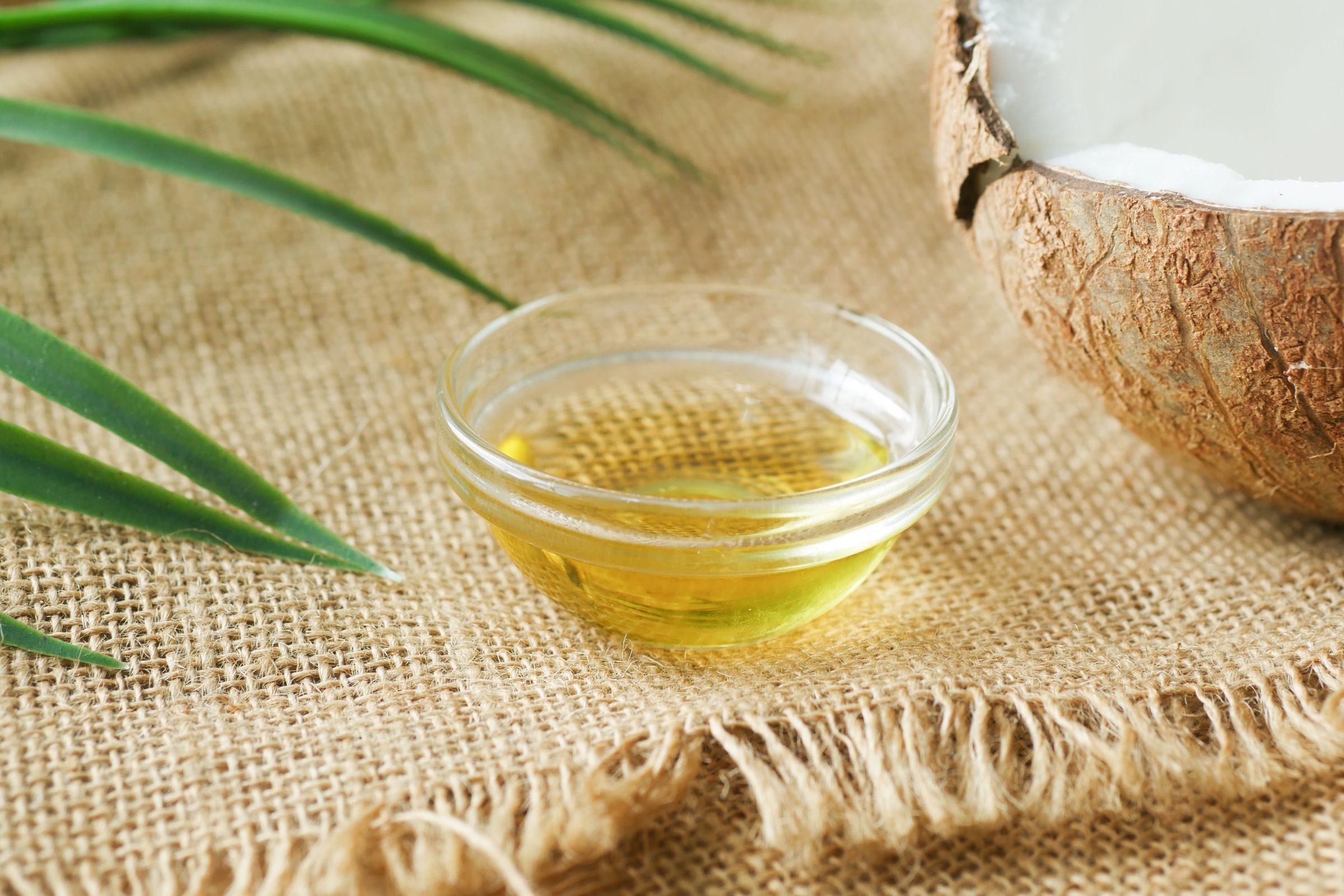 A glass bowl of coconut oil beside half a coconut